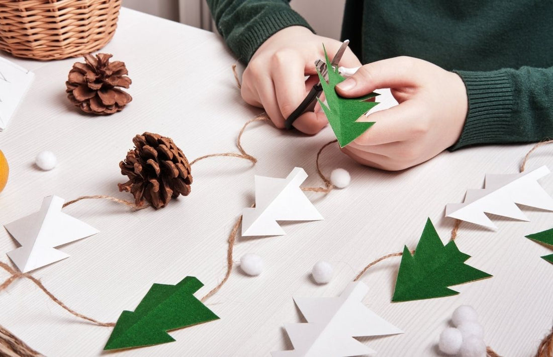 Un enfant fait un atelier et découpe du papier pour faire une guirlande de sapin et des décorations avec des pommes de pin